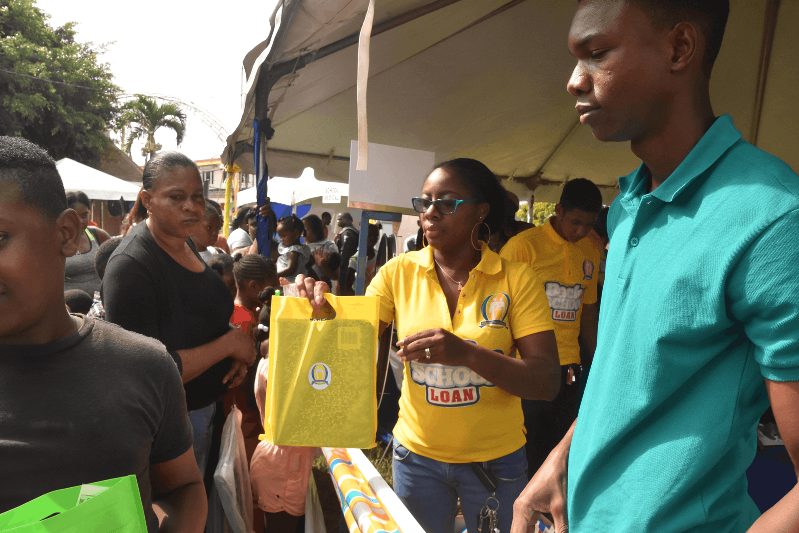An MCCU team member in a yellow Back to School Loan shirt hands a school-loan gift bag to a young man at the Back to School Extravaganza.